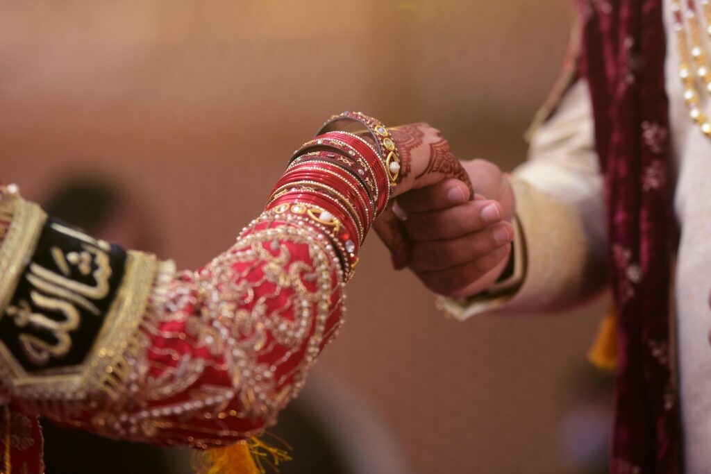 Close-up of a couple's hands in traditional wedding attire adorned with henna and jewelry.