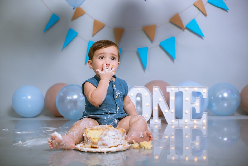 Cute baby enjoying a first birthday cake smash with balloons and decorations.