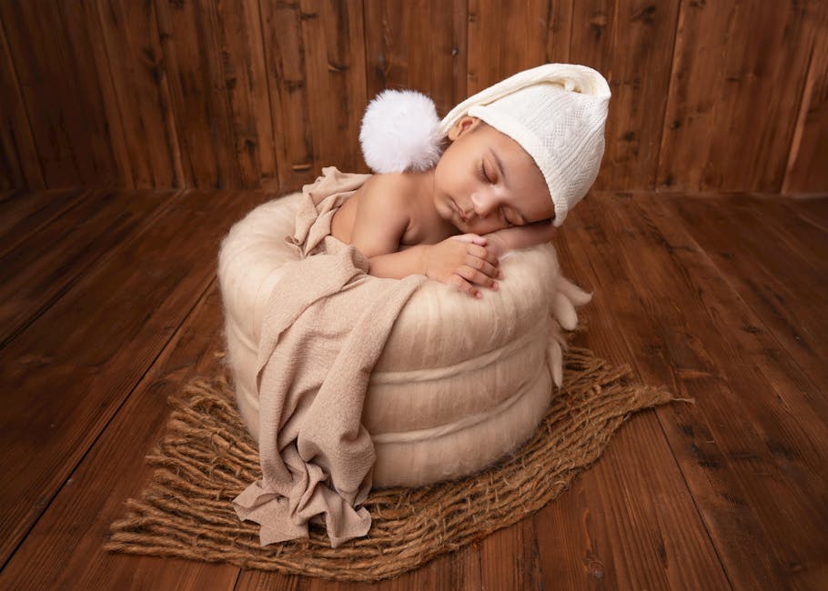 A serene newborn baby naps in a fluffy basket, wrapped in a blanket with a knit hat.